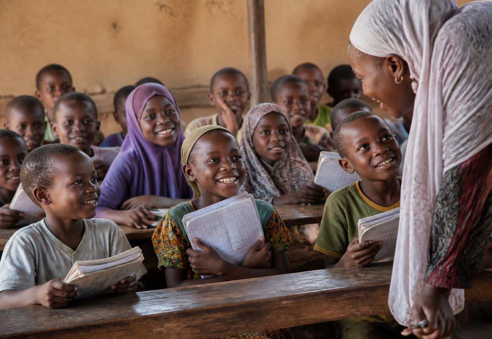 Pupils in a rural Nigerian classroom holding their exercise books beside their teacher
